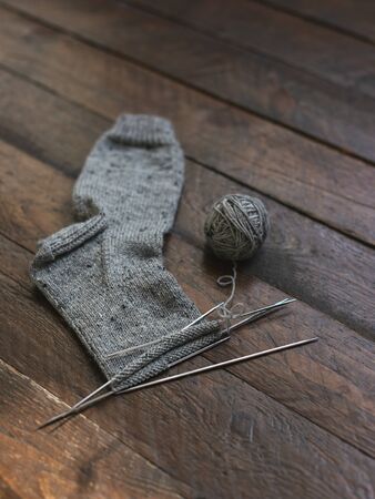 Hand knitted sock with needles and grey yarn ball on dark wooden background. Concept for handmade and hugge slow life.の写真素材