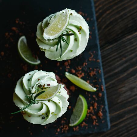Tasty chocolate cupcake with buttercream icing and lime slices on a wooden table. Dark background.  Top view. Place for text.の写真素材