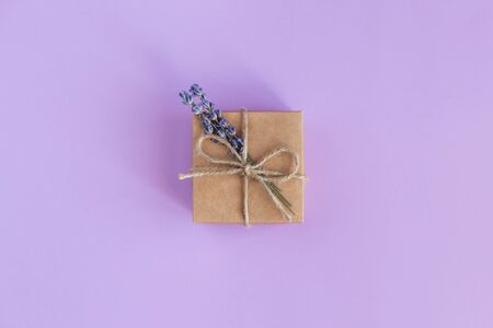 Craft gift box with small lavender bouquet on pastel violet background. Holiday eco-friendly concept. Place for text. Flat lay.の写真素材