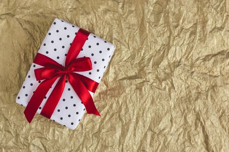 Gift box wrapped in black polka-dot white paper with red bow on golden foil  background. Holiday concept. Place for text.の写真素材