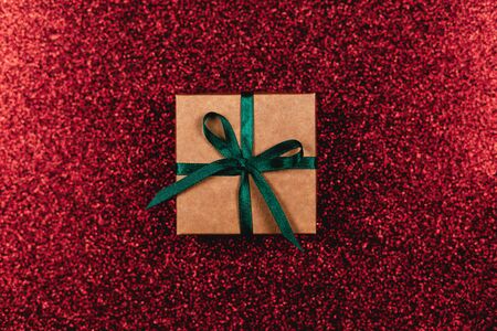 Craft gift box with green bow on dark red sparkle background. Holiday concept. Flat lay.の写真素材