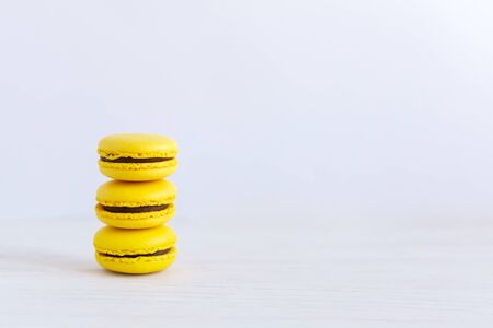 Three yellow french macarons on a wooden table. Banana macarons with chocolate cream. White background. Place for text. Close-up.の写真素材