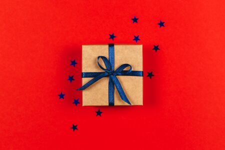 Craft gift box with blue bow on red background with blue stars. Holiday concept. Flat lay.の写真素材