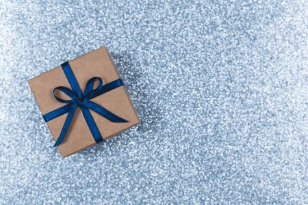 Craft gift box with blue bow on sparkle light blue background. Holiday concept. Flat lay. Place for text.の写真素材