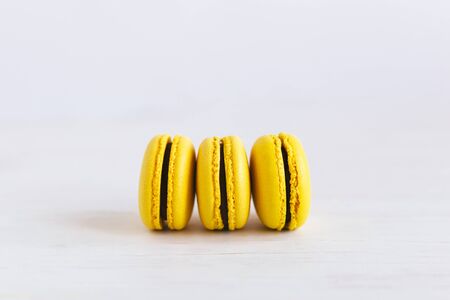Three yellow french macarons on a wooden table. Banana macarons with chocolate cream. White background. Close-up.の写真素材