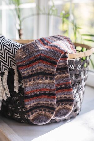 A pair of hand knitted multi-colored socks in a basket by the window on a sunny day. Close-up.の写真素材
