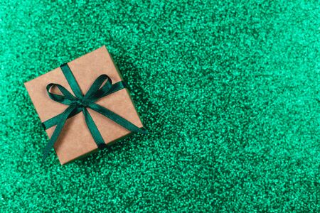 Craft gift box with green bow on sparkle green background. Holiday concept. Flat lay. Place for text.の写真素材