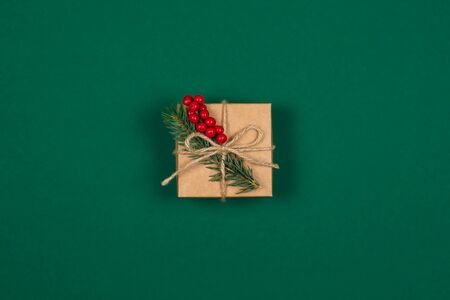 Craft gift box with spruce branch and red berries on green background. Holiday eco-friendly concept. Place for text. Flat lay.の写真素材