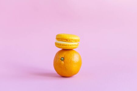 Tasty french macarons and tangerine on pink background.  Close-up. Place for text.の写真素材