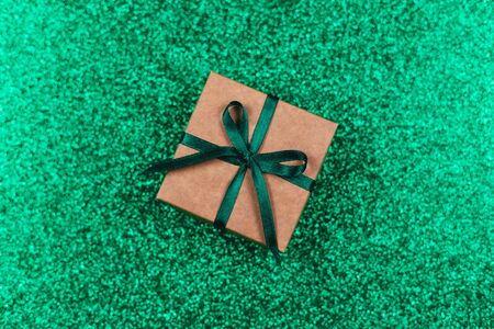 Craft gift box with green bow on sparkle green background. Holiday concept. Flat lay. Place for text.の写真素材