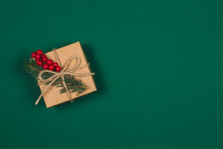 Craft gift box with spruce branch and red berries on green background. Holiday eco-friendly concept. Place for text. Flat lay.の写真素材