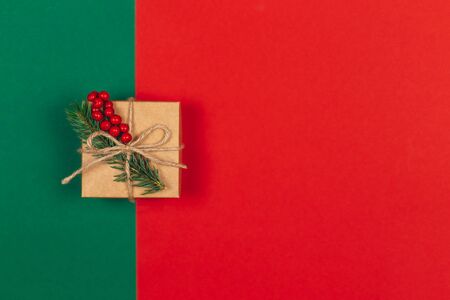 Craft gift box with spruce branch and red berries on green and red background. Holiday eco-friendly concept. Place for text. Flat lay.の写真素材