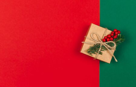 Craft gift box with spruce branch and red berries on green and red background. Holiday eco-friendly concept. Place for text. Flat lay.の写真素材