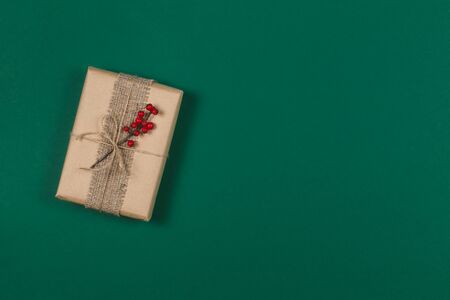 Craft gift box with branch of red berries on dark green background. Holiday eco-friendly concept. Place for text. Flat lay.の写真素材