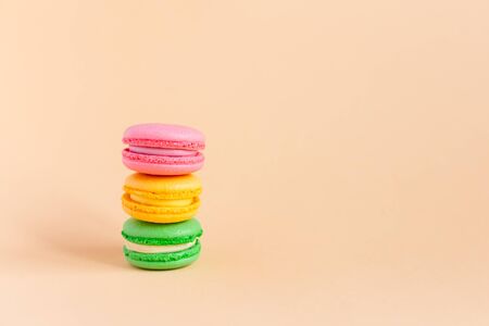 Three tasty french macarons on peach pastel background.  Pink, yellow and green macarons. Close-up. Place for text.の写真素材