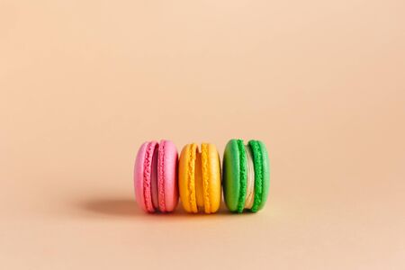 Three tasty french macarons on peach pastel background.  Pink, yellow and green macarons. Close-up. Place for text.の写真素材
