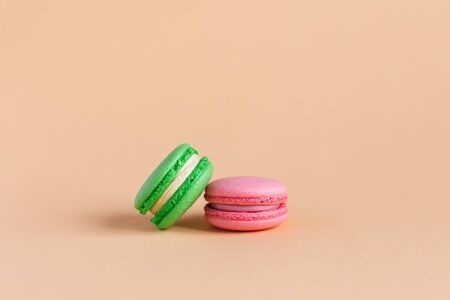Two tasty french macarons on peach pastel background.  Pink and green macarons. Close-up. Place for text.の写真素材