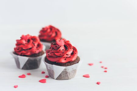 Valentine cupcakes in red color, decorated with sweet hearts on white wooden table. Place for text.の写真素材