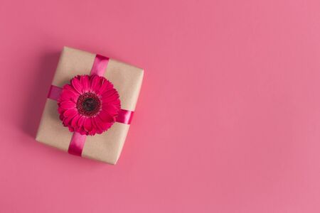 Craft gift box with pink flower and ribbon on a pink background. Valentine's or mother's day concept. Place for text. Flat lay.の写真素材
