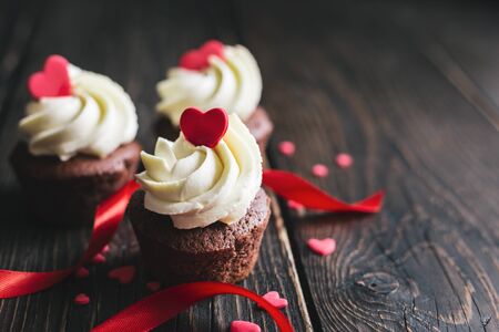 Valentine cupcakes, decorated with sweet hearts with ribbon on dark wooden table. Place for text.の写真素材