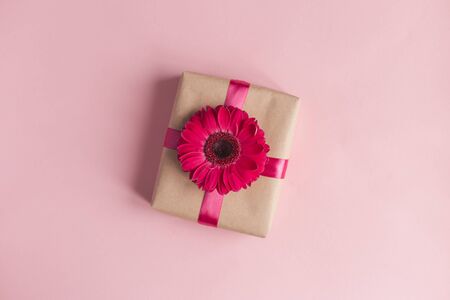 Craft gift box with pink flower and ribbon on a pastel pink background. Valentine's or mother's day concept. Place for text. Flat lay.の写真素材