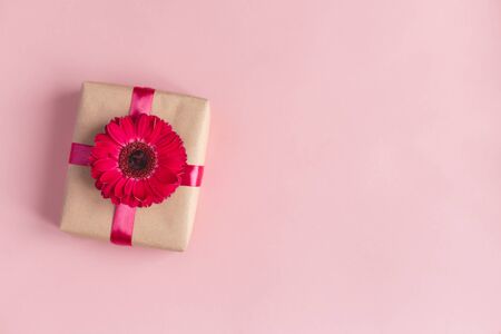 Craft gift box with pink flower and ribbon on a pastel pink background. Valentine's or mother's day concept. Place for text. Flat lay.の写真素材