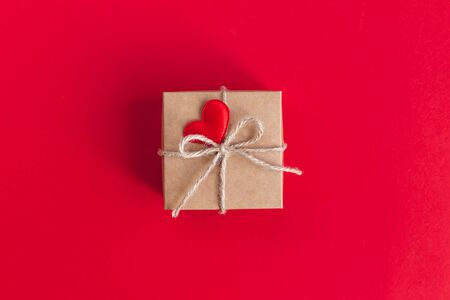Craft gift box with red heart on a red background. Holiday concept for Valentine day. Place for text. Flat lay.の写真素材