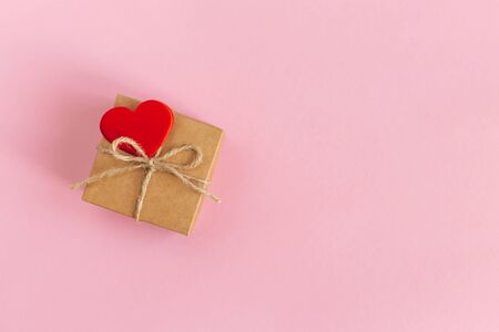 Craft gift box with red heart on a pink pastel background. Holiday concept for Valentine's day. Place for text. Flat lay.の写真素材