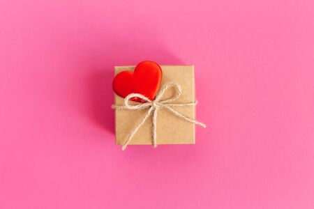 Craft gift box with red heart on a bright pink background. Holiday concept for Valentine's day. Place for text. Flat lay.の写真素材