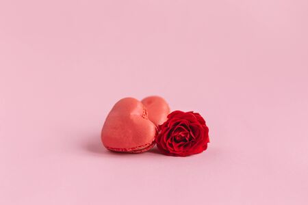 Tasty french heart-shaped macaroons with red rose on a pink pastel background.  Concept for Valentine's Day. Place for text.の写真素材