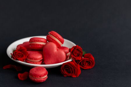 Tasty french macarons with red roses on a black background. Concept for Valentine's day. Place for text.の写真素材