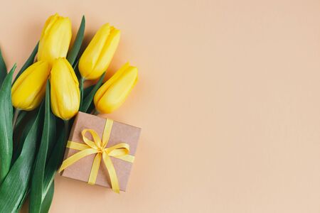 Tender yellow tulips with gift box on pastel peach background. Greeting card for Mother's day. Place for text. の写真素材