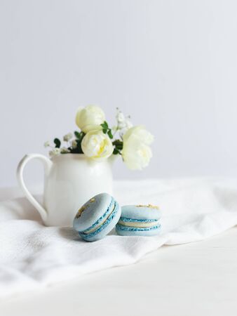 Tasty blue  french macarons and jar with cream roses on a white woodenの写真素材