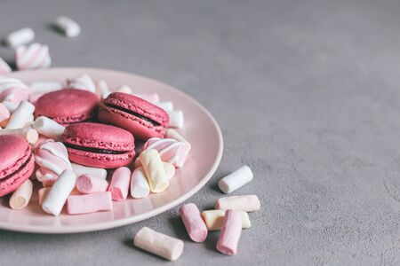 Tasty pink french macaroons and marshmallows on a plate. Grey background. Place for text.