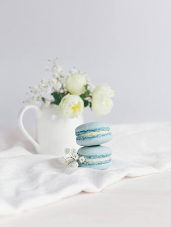 Tasty blue  french macarons and jar with cream roses on a white wooden background.  Place for text.の写真素材