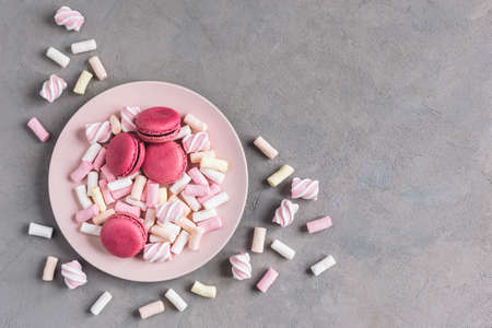 Tasty pink french macaroons and marshmallows on a plate. Grey background. Place for text.