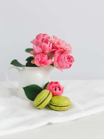 Two tasty French macarons and a jar with beautiful roses on a white background. Place for text.の写真素材