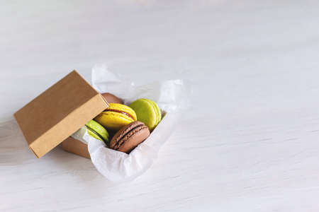 Tasty french macarons in a box on white wooden table. Place for text.
