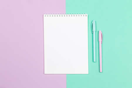 Notebook with blank page and two pens on a violet and turquoise background. Flat lay. Place for...