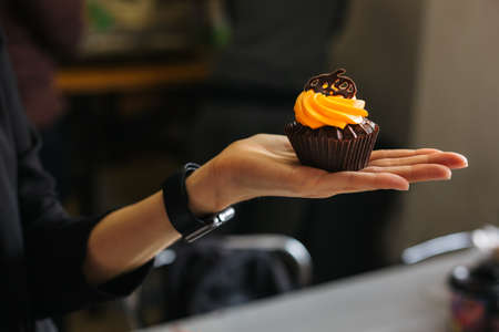 Tasty chocolate cupcake with orange cream, decorated with chocolate pumpkin in a girl's hand. Sweets...