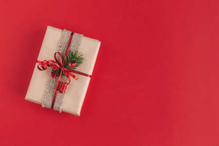 Craft gift box with spruce branch on a red background. Holiday eco-friendly concept. Place for text....