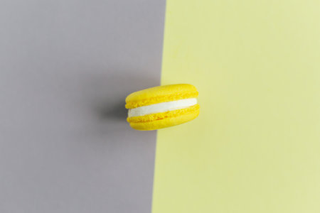 Tasty french yellow macaroon on a gray and yellow background. Place for text. Flat lay.