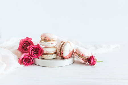 Tasty french macaroons with pink roses on a plate. White background. Place for text.の写真素材