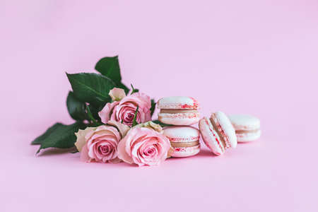 Tasty french macaroons with pink roses on a pink pastel background. Place for text.の写真素材