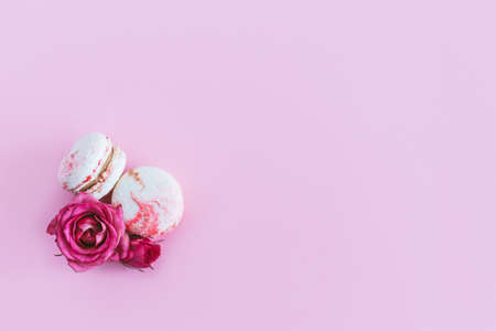 Tasty french macaroons with pink roses on a pink pastel background. Flat lay. Place for text.の写真素材