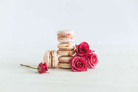 Tasty french macaroons with pink roses on a white wooden background. Place for text.の写真素材