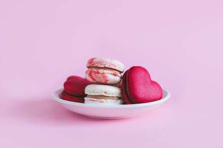 Tasty french macaroons on a white plate. Pink pastel background. Place for text.