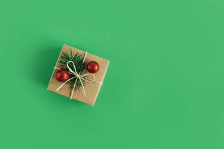 Craft gift box with spruce branch and red balls on a green background. Holiday concept. Place for text. Flat lay.の写真素材