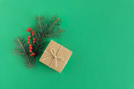 Craft gift box with spruce branch and red berries on a green background. Holiday concept. Place for text. Flat lay.の写真素材