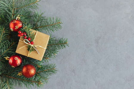 Craft gift box with spruce branch and red balls on a gray background. Holiday concept. Place for text. Flat lay.の写真素材